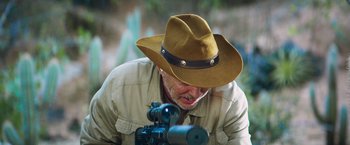 A man with a hat on looking at a rifle