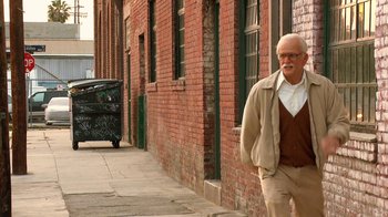 Movie still from “Jackass Presents: Bad Grandpa” (2013), directed by Jeff Tremaine – An older man walking down the sidewalk in front of a brick building; Wide shot, Low angle