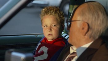 Movie still from “Jackass Presents: Bad Grandpa” (2013), directed by Jeff Tremaine – A young boy wearing a superman cape sitting next to an older man; Close Up shot, Over the shoulder angle