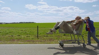 Movie still from “Jackass Presents: Bad Grandpa” (2013), directed by Jeff Tremaine – A man sitting in a shopping cart on the side of the road; Wide shot, Low angle