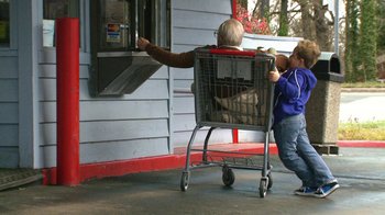 Movie still from “Jackass Presents: Bad Grandpa” (2013), directed by Jeff Tremaine – An older woman pushing a shopping cart while a young boy holds her arm out; Wide shot, Low angle