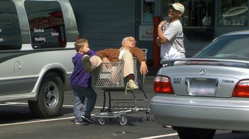 Movie still from “Jackass Presents: Bad Grandpa” (2013), directed by Jeff Tremaine – Two men and a boy are sitting in a shopping cart in a parking lot; Wide shot, High angle