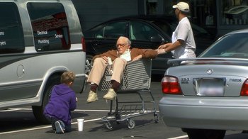 Movie still from “Jackass Presents: Bad Grandpa” (2013), directed by Jeff Tremaine – An older man sitting in a shopping cart in a parking lot; Wide shot, High angle