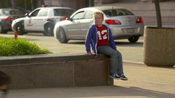 Movie still from “Jackass Presents: Bad Grandpa” (2013), directed by Jeff Tremaine – A young boy sitting on the side of the street; Wide shot, Over the shoulder angle