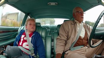 A boy and an old man sitting in the back of a car