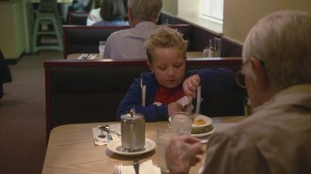 Movie still from “Jackass Presents: Bad Grandpa” (2013), directed by Jeff Tremaine – A little boy sitting at a table with a plate of food; Medium shot, Over the shoulder angle