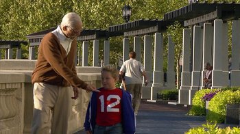 Movie still from “Jackass Presents: Bad Grandpa” (2013), directed by Jeff Tremaine – An older man is helping a young boy to walk; Medium shot, Over the shoulder angle