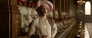 Movie still from “Bajirao Mastani” (2015), directed by Sanjay Leela Bhansali – A man with a mustache and a pink hat is standing in front of a crowd; Medium shot, Low angle