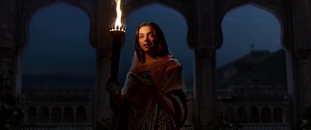 A woman holding a torch in front of an archway at night