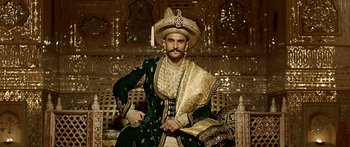 Movie still from “Bajirao Mastani” (2015), directed by Sanjay Leela Bhansali – A man in a green and gold outfit sitting on a couch; Medium shot, Low angle