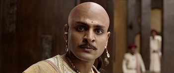 Movie still from “Bajirao Mastani” (2015), directed by Sanjay Leela Bhansali – A man with a bald head wearing a necklace and earrings; Close Up shot, Over the shoulder angle