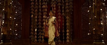 A woman in a white sari is standing in front of a curtain