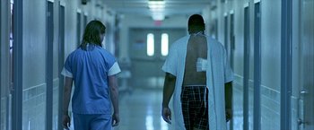 Movie still from “Ballast” (2008), directed by Lance Hammer – A man in a hospital gown walks down a hallway with a nurse; Medium shot, Low angle