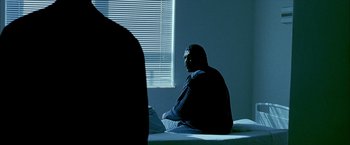 Movie still from “Ballast” (2008), directed by Lance Hammer – A man sitting on top of a bed next to a window; Medium shot, Over the shoulder angle