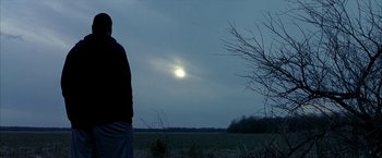 Movie still from “Ballast” (2008), directed by Lance Hammer – A man standing in a field looking at the sun; Medium shot, Low angle