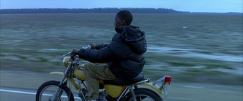 Movie still from “Ballast” (2008), directed by Lance Hammer – A man riding a motorcycle down a road; Medium shot, Over the shoulder angle