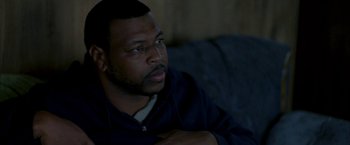 Movie still from “Ballast” (2008), directed by Lance Hammer – A man sitting on top of a couch in a room; Close Up shot, High angle