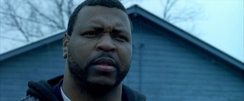 Movie still from “Ballast” (2008), directed by Lance Hammer – A man's face in front of a building; Close Up shot, Low angle