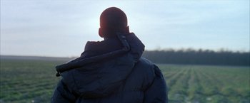 Movie still from “Ballast” (2008), directed by Lance Hammer – A man wearing a black jacket standing in a field; Medium shot, Over the shoulder angle