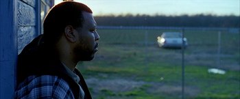 Movie still from “Ballast” (2008), directed by Lance Hammer – A man standing next to a car on a field; Close Up shot, Over the shoulder angle