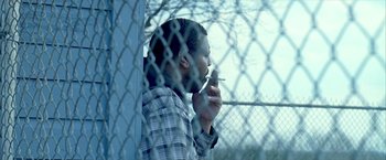Movie still from “Ballast” (2008), directed by Lance Hammer – A man is smoking a cigarette behind a chain link fence; Close Up shot, Low angle