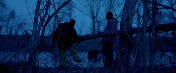 Movie still from “Ballast” (2008), directed by Lance Hammer – Two people and a dog are standing in the woods; Wide shot, Over the shoulder angle