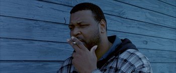 Movie still from “Ballast” (2008), directed by Lance Hammer – A man is smoking a cigarette in front of a blue wall; Close Up shot, Low angle