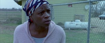 Movie still from “Ballast” (2008), directed by Lance Hammer – A woman with a head scarf is sitting in front of a chain link fence; Close Up shot, High angle