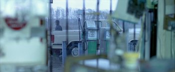 Movie still from “Ballast” (2008), directed by Lance Hammer – A man is sitting in the back of a pick - up truck at a gas station; Wide shot, Over the shoulder angle