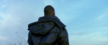 Movie still from “Ballast” (2008), directed by Lance Hammer – A man wearing a black jacket looking out at the sky; Medium shot, Low angle