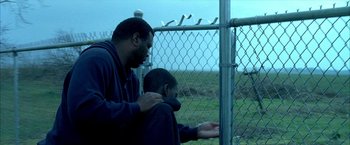 Movie still from “Ballast” (2008), directed by Lance Hammer – A man and a boy sitting next to a fence; Medium shot, Over the shoulder angle