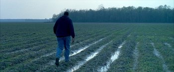 Movie still from “Ballast” (2008), directed by Lance Hammer – A man walking across a field in the rain; Extreme Wide shot, High angle