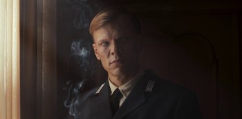 Movie still from “Dark” (2017), created by Baran bo Odar – A man in a uniform is smoking a cigarette; Close Up shot, Low angle