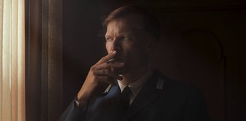 Movie still from “Dark” (2017), created by Baran bo Odar – A man smoking a cigarette while wearing a suit and tie; Close Up shot, Low angle