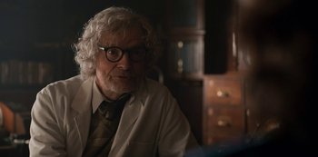 Movie still from “Dark” (2017), created by Baran bo Odar – An older man in a white lab coat and tie; Close Up shot, Over the shoulder angle