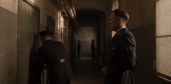 Movie still from “Dark” (2017), created by Baran bo Odar – Two men in uniform are standing in a hallway; Medium shot, Over the shoulder angle