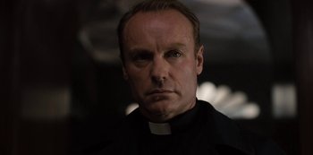 Movie still from “Dark” (2017), created by Baran bo Odar – A man wearing a priest's outfit and a black shirt; Close Up shot, Low angle