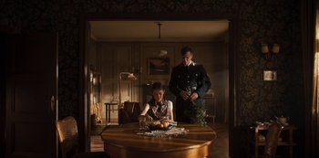 Movie still from “Dark” (2017), created by Baran bo Odar – A woman sitting at a table with a man standing next to her; Wide shot, Low angle