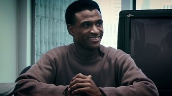 Movie still from “Bamboozled” (2000), directed by Spike Lee – A man sitting at a table with his hands clasped together; Close Up shot, High angle