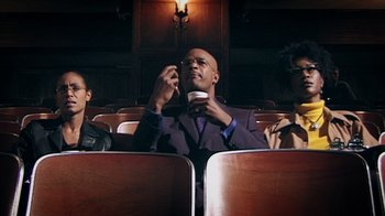 Movie still from “Bamboozled” (2000), directed by Spike Lee – A man sitting in a movie theater with two other people; Medium shot, Low angle