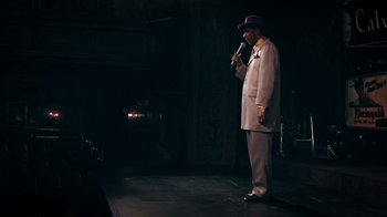 Movie still from “Bamboozled” (2000), directed by Spike Lee – A man standing on a stage holding a microphone; Wide shot, High angle