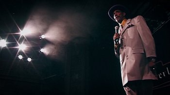 Movie still from “Bamboozled” (2000), directed by Spike Lee – A man with a microphone on a stage with smoke; Medium shot, Low angle
