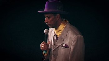 Movie still from “Bamboozled” (2000), directed by Spike Lee – A man wearing a purple hat holding a microphone; Close Up shot, Low angle