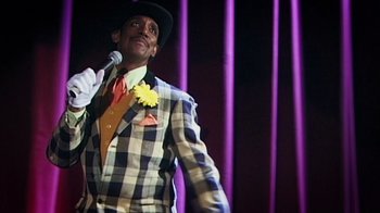 Movie still from “Bamboozled” (2000), directed by Spike Lee – A man wearing a suit and tie holding a microphone; Medium shot, Low angle