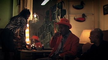 Movie still from “Bamboozled” (2000), directed by Spike Lee – A man in a red jacket and orange hat drinking a drink; Medium shot, Low angle