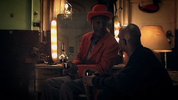 Movie still from “Bamboozled” (2000), directed by Spike Lee – A man in a red jacket and a man in a red hat are talking; Medium shot, Over the shoulder angle