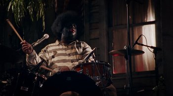 Movie still from “Bamboozled” (2000), directed by Spike Lee – A man with a black afro playing drums; Medium shot, Low angle