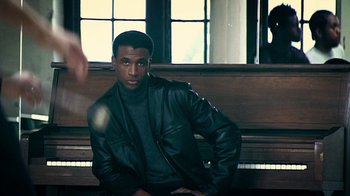 Movie still from “Bamboozled” (2000), directed by Spike Lee – A man sitting on top of a bench in a room; Medium shot, Low angle