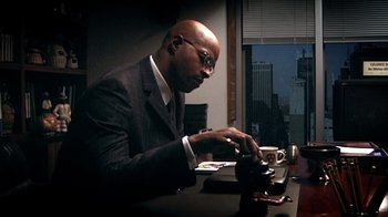Movie still from “Bamboozled” (2000), directed by Spike Lee – A man sitting at a table with a cup of coffee; Medium shot, Low angle