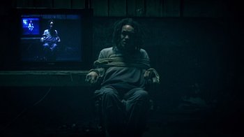 Movie still from “Bamboozled” (2000), directed by Spike Lee – A man with dreadlocks tied to a chair in front of a television; Medium shot, High angle
